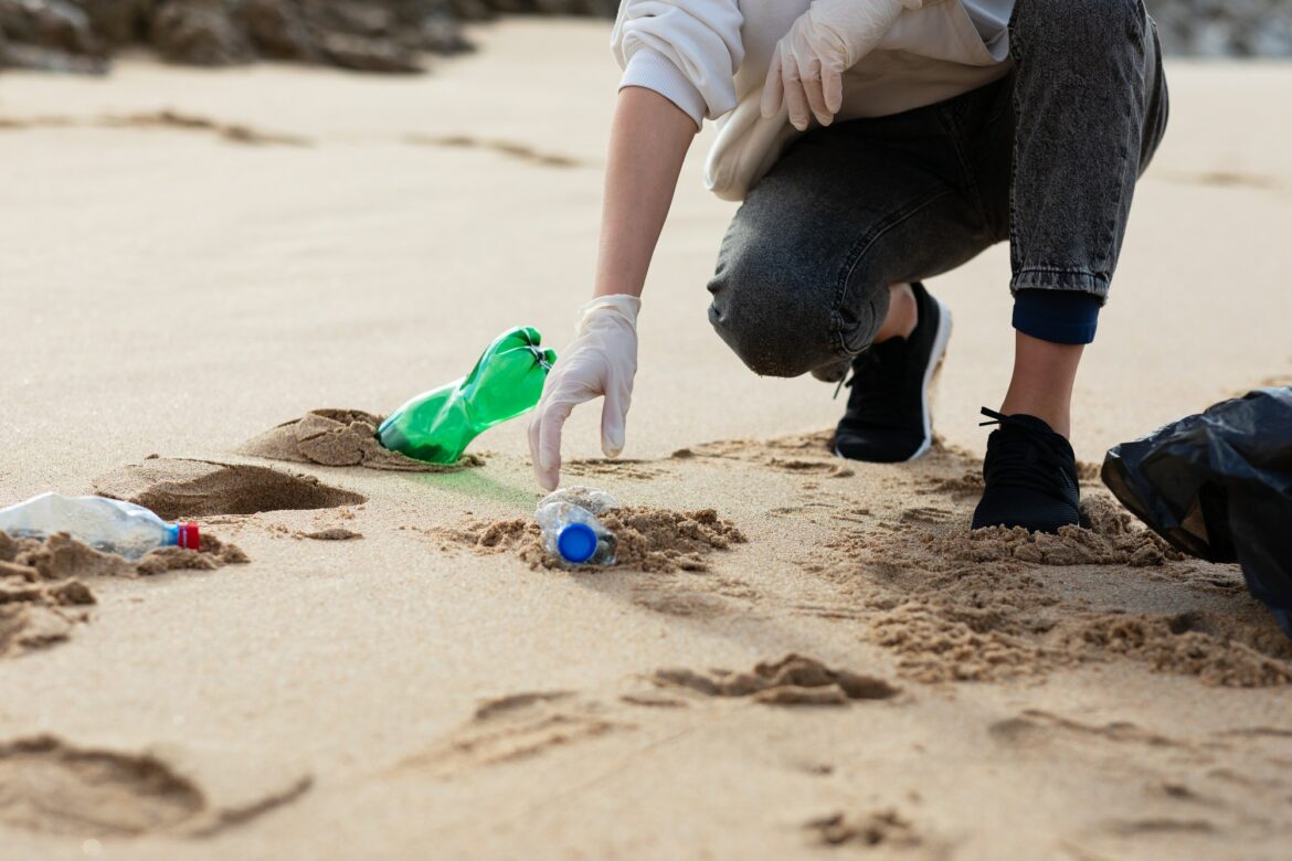 Female volunteer picking up trash and plastics, cleaning beach with a garbage bag, copy space Female volunteer picking up trash and plastics, cleaning beach with a garbage bag, copy space